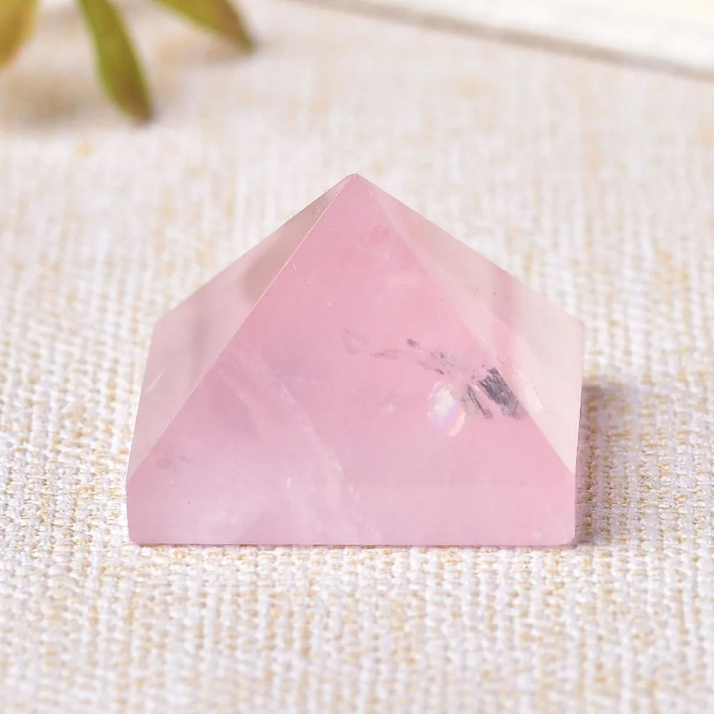 Pink rose quartz pyramid crystal on a beige textured surface.
