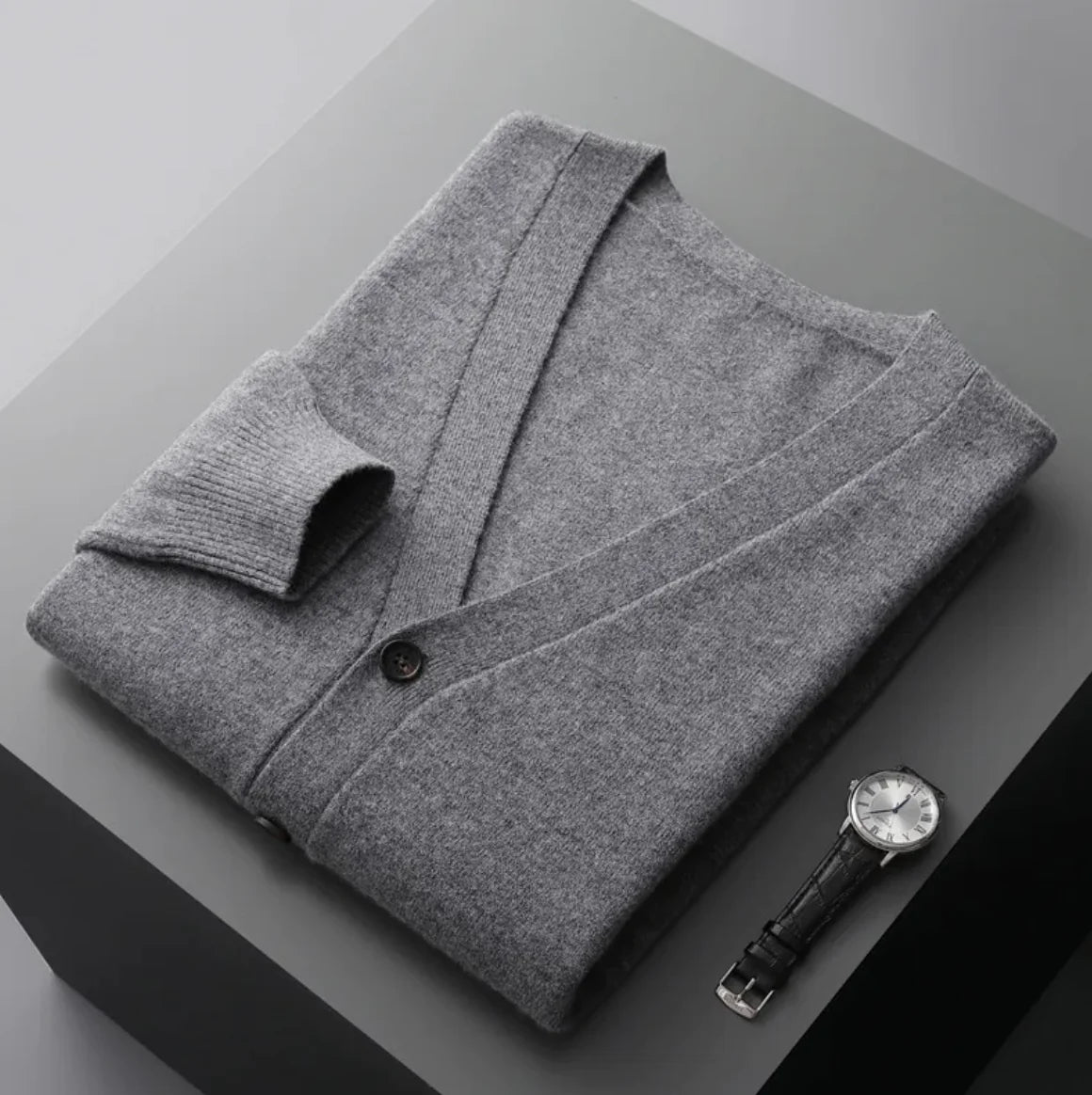 A neatly fold shirt on a black box with a black leather watch beside it