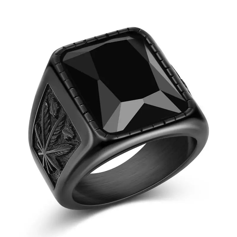 This image shows a stylish men's ring featuring a large black gemstone in a rectangular cut, surrounded by a black metal band. One side of the ring is detailed with an intricate carving of a cannabis leaf, adding a unique touch to the design. The overall look is bold and modern.