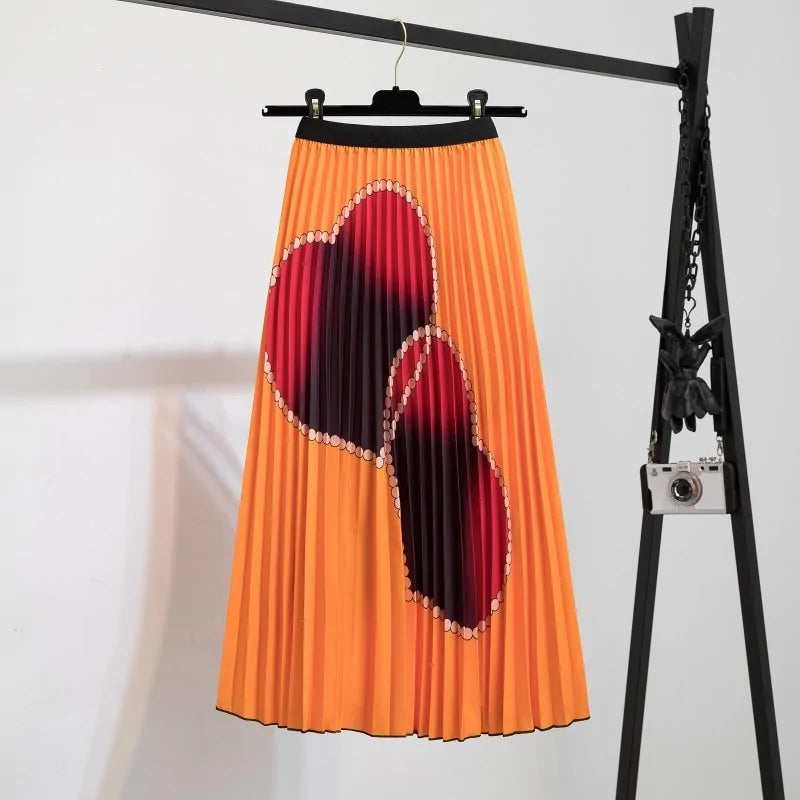 Pleated midi skirt with a gradient design, transitioning from dark black at the waistband to a soft blush pink at the hem, hanging on a black clothing rack next to a vintage-style camera.