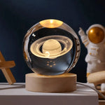 Glowing crystal ball lamp on a wooden base with an etched Saturn-and-rings design, with an astronaut figure in the background.