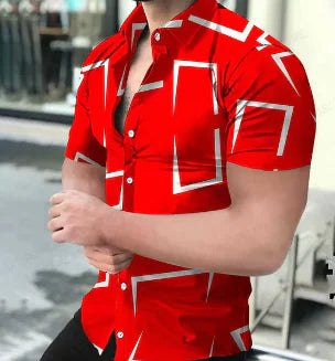 A muscular man wearing a stylish short-sleeved button-up shirt. The upper part of the shirt is purple with a geometric pattern resembling a honeycomb, while the lower part is solid black. The shirt is partially unbuttoned, revealing part of his chest. The background appears to be an outdoor urban setting with blurred reflections in a glass window and some chairs visible.