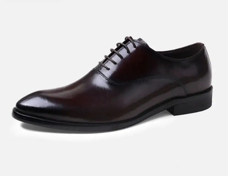 A pair of elegant burgundy leather loafers with a glossy finish. The shoes feature gold-toned metal horsebit detailing across the uppers and are displayed with wooden shoe trees inserted. They have a sleek, elongated silhouette with subtle stitching along the toe cap. The loafers are placed on a dark surface, partially framed by a wooden picture frame, emphasizing their classic and sophisticated style.