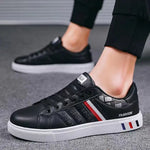 A pair of black low-top sneakers with white soles, worn by a person dressed in black joggers. The shoes feature red, white, and blue side stripes, “SPORT” lettering on the side panels, and the word “FASHION” near the heel.
