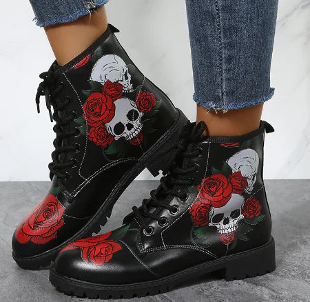 Black boots with skull and rose designs worn with jeans on a neutral background