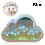 A blue cloud-shaped decorative mirror or night light with a soft pastel frame and an illuminated floral scene inside featuring glowing blue tulip-like flowers. A small inset image at the top left shows the item displayed on a tabletop with miniature figurines, and the word “Blue” appears in bold black text at the top right against a plain light background.