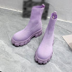 A pair of chunky lavender sock boots with thick platform soles and ribbed knit uppers, displayed on a gray tiled floor against a light-colored wall.