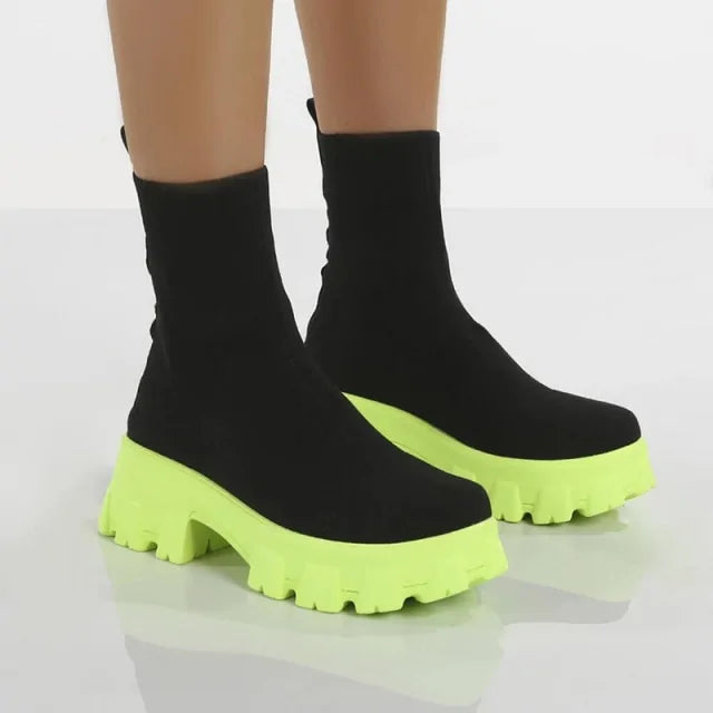 A pair of chunky lavender sock boots with thick platform soles and ribbed knit uppers, displayed on a gray tiled floor against a light-colored wall.