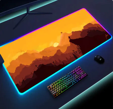 Gaming desk setup with a large RGB-lit mouse pad featuring an orange-hued landscape design, a colorful backlit keyboard, and a gaming mouse, all illuminated by LED lights.