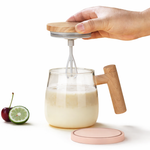 Hand using a milk frother to create foam in a glass with wooden handles on a white background.