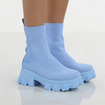 A pair of chunky lavender sock boots with thick platform soles and ribbed knit uppers, displayed on a gray tiled floor against a light-colored wall.