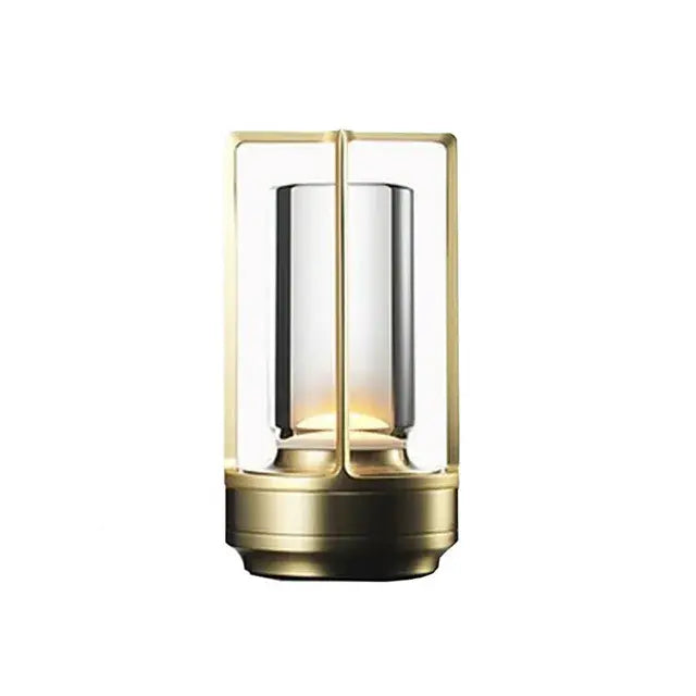 Modern tabletop lantern with a black frame and clear cylindrical glass shade, emitting a warm light on a wooden surface.
