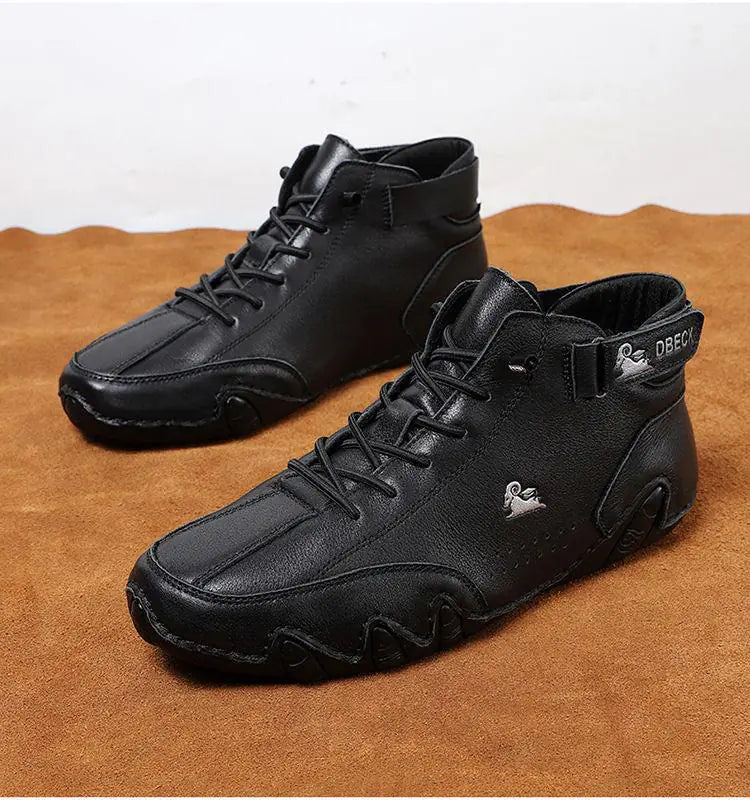 A single brown casual ankle boot designed with a rugged, stitched leather upper and a unique black rubber sole with wave-like contours. The shoe features both laces and a hook-and-loop strap for added support, along with a small black gecko logo on the side. It's displayed tilted upward on a white pedestal, emphasizing its craftsmanship and durability.