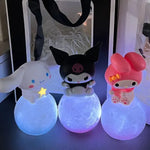 Three cute, colorful characters from a popular Japanese cartoon series, sitting on glowing, pastel-colored balls. Each character has its own unique design: a white bunny with a star, a black skull-themed figure, and a pink bunny with a bow, all lit up.