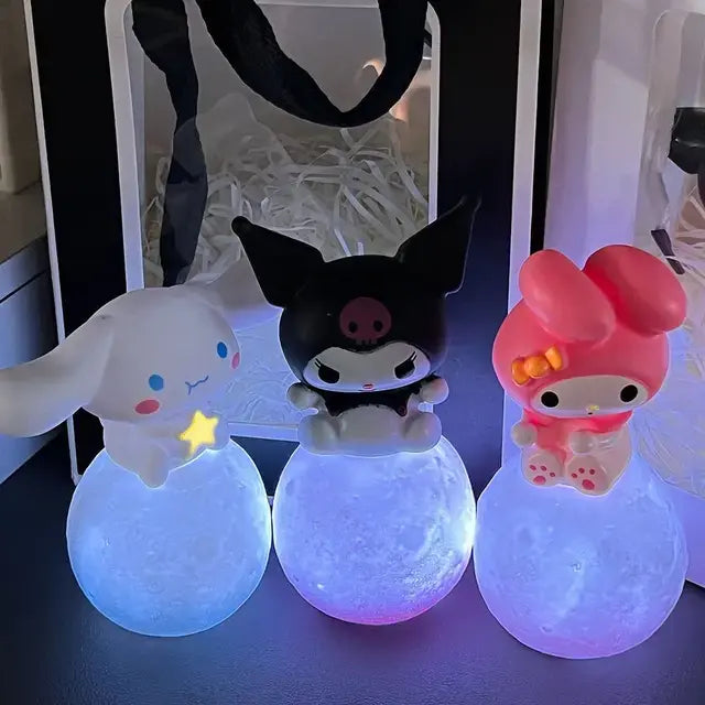 Three cute, colorful characters from a popular Japanese cartoon series, sitting on glowing, pastel-colored balls. Each character has its own unique design: a white bunny with a star, a black skull-themed figure, and a pink bunny with a bow, all lit up.