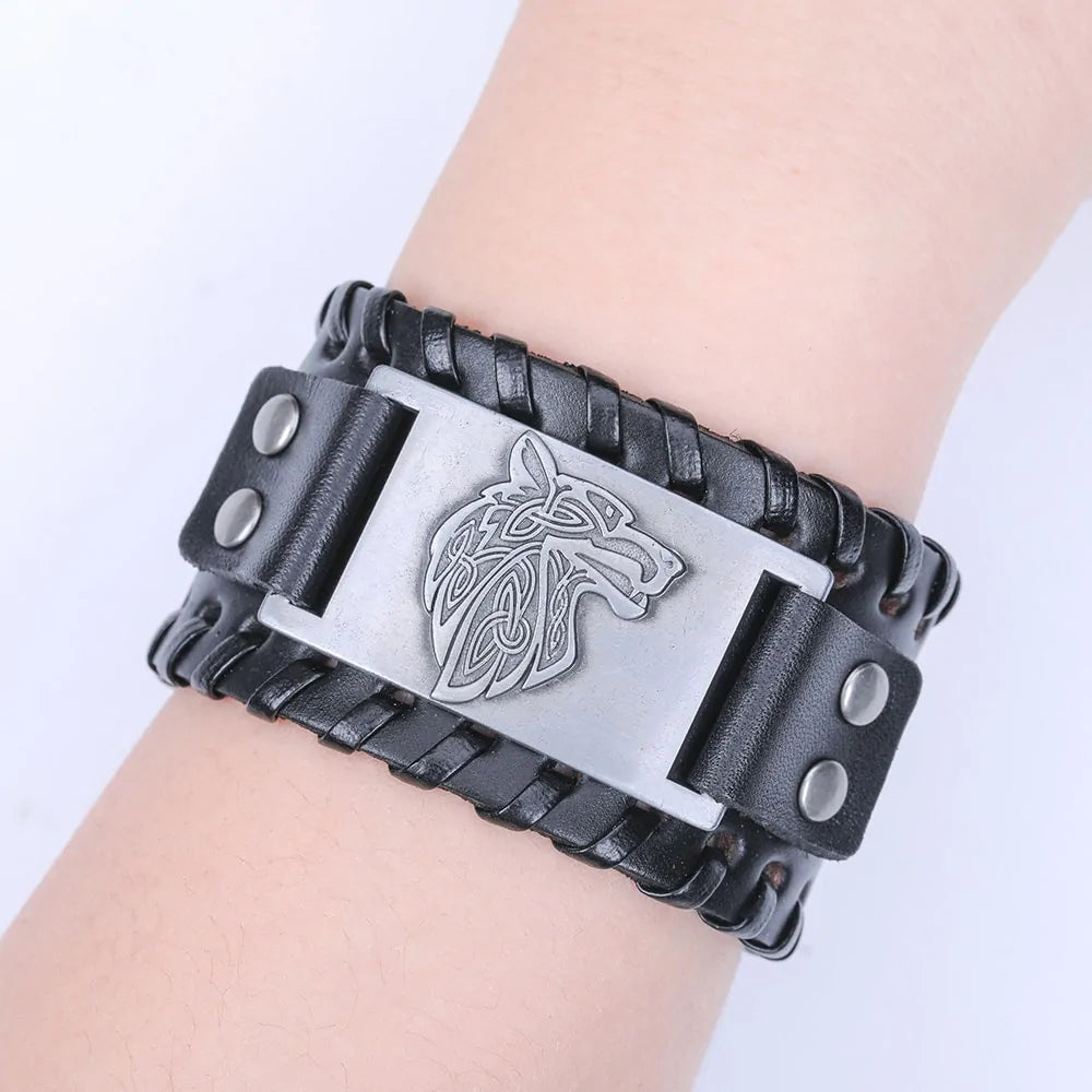 Black braided leather wristband bracelet with a rectangular silver-toned plate engraved with a Celtic-style wolf head, fastened with snap buttons.