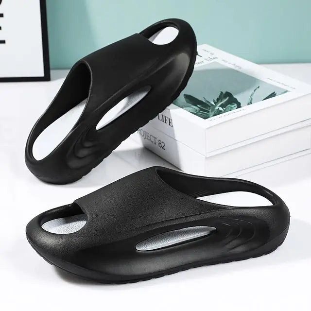 A pair of stylish black slip-on sandals with purple cushioned insoles, featuring cutout designs on the sides and toes, displayed on a white surface next to stacked books.