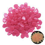 pile of small, smooth, pink teardrop-shaped pebbles on a white background, with a small inset photo showing the same pieces glowing a pale orange/yellow in the dark.