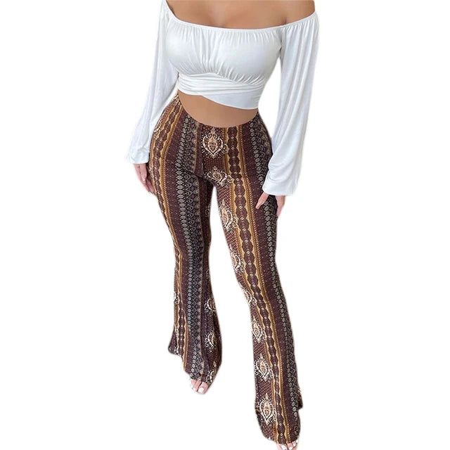 Woman wearing a black crop top and high-waisted, flared bohemian print pants with a mix of geometric and floral patterns in shades of purple, white, and maroon, posing with one hand on her hip