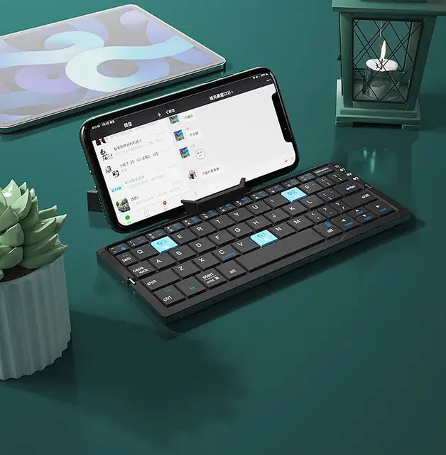 Foldable black Bluetooth keyboard with a smartphone dock, shown on a desk with a phone in place.