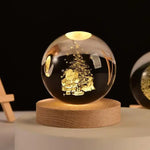 Glass crystal ball lamp engraved with the solar system, glowing on a wooden base with a power cord, set on a desk with an astronaut figurine in the background.