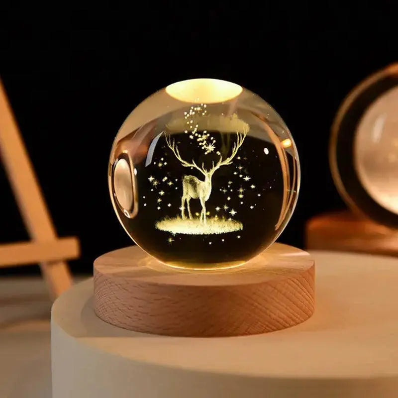 Crystal ball night light with a laser-etched deer and stars inside, glowing warm white on a wooden base in a dim room.
