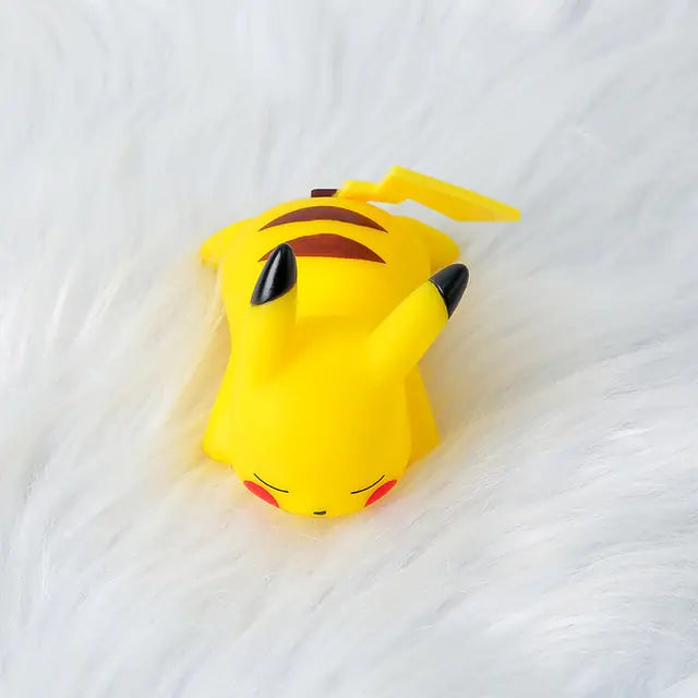 Small yellow Pikachu figurine or toy lying on a white fluffy surface, showing its black-tipped ears, red cheeks, and striped back.