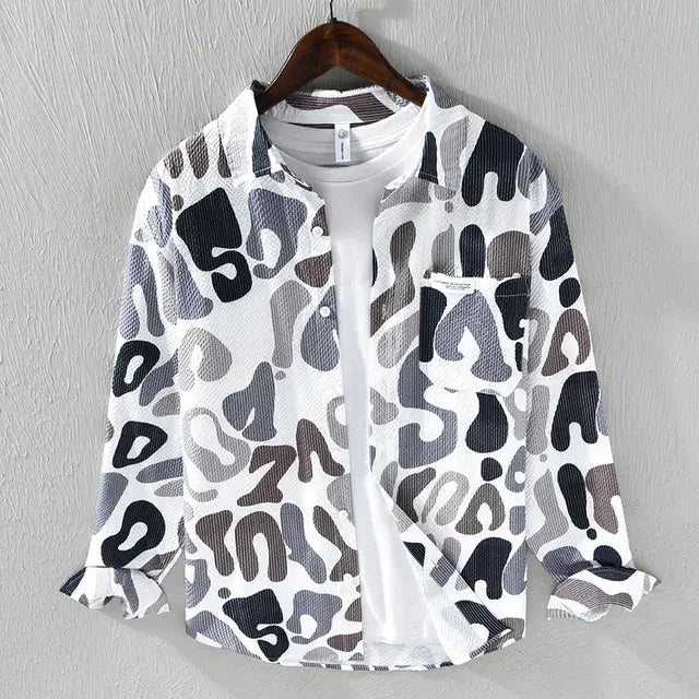This is a stylish long-sleeve button-up shirt with a white base and an artistic abstract print in gray tones. The lightweight, textured fabric gives it a breezy, casual feel, making it perfect for layering over a t-shirt, as shown in the image. It also features a front pocket with a small label detail that adds a modern touch.