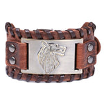The image shows a brown leather bracelet with a woven design and metal embellishments. The centerpiece is a silver-colored metal plate featuring a wolf head design, which adds a rugged, tribal look to the bracelet.
