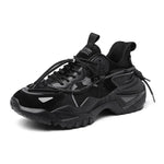 Black chunky athletic sneaker with layered mesh and synthetic panels, reflective accents, thick rugged outsole, and long black laces.