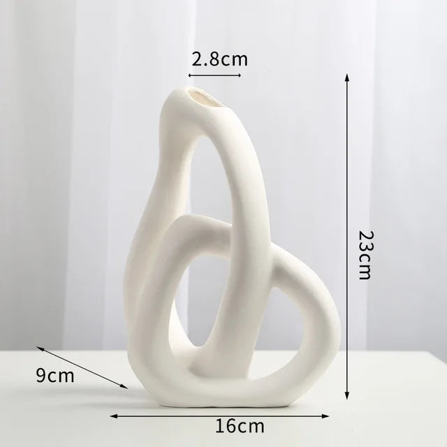 Abstract white ceramic vase with intertwined loop design, shown with labeled dimensions: 23 cm tall, 16 cm wide, 9 cm deep, and a 2.8 cm opening.