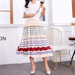 Pleated midi skirt with a gradient design, transitioning from dark black at the waistband to a soft blush pink at the hem, hanging on a black clothing rack next to a vintage-style camera.