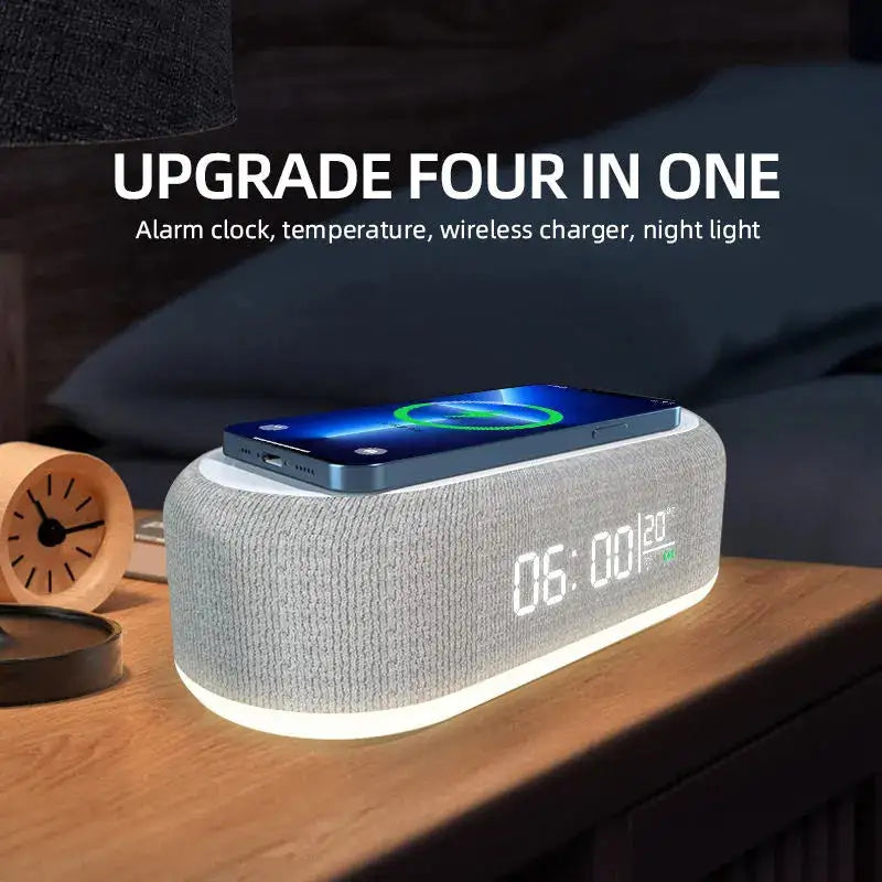 Promotional image of a gray fabric-covered bedside alarm clock with a glowing base and digital display reading “06:00” and “23°C,” with a smartphone resting on top on a wireless charging pad; headline text reads “UPGRADE FOUR IN ONE” with “Alarm clock, temperature, wireless charger, night light.