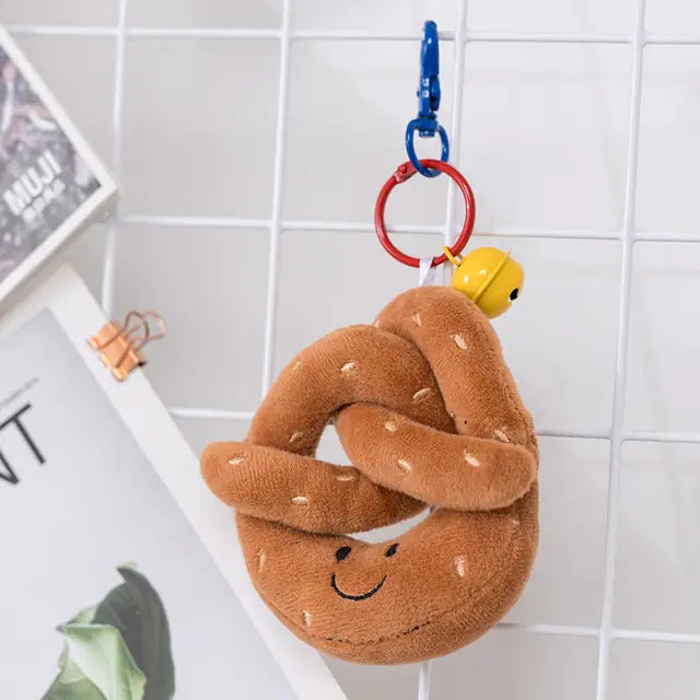 Soft pretzel-shaped plush keychain with a smiling face, hanging from a blue clip and red ring.
