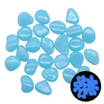 A group of light-blue glow-in-the-dark pebbles scattered on a white background, with an inset showing them glowing bright blue in the dark.
