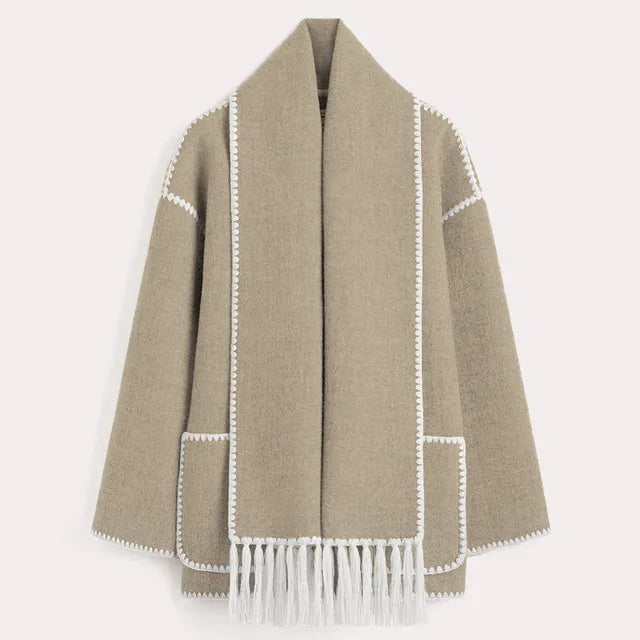 Dark wool coat with white blanket stitch trim, featuring front buttons, large patch pockets, and an attached matching scarf with fringe detailing draped over the shoulder. The coat is displayed against a plain white background.