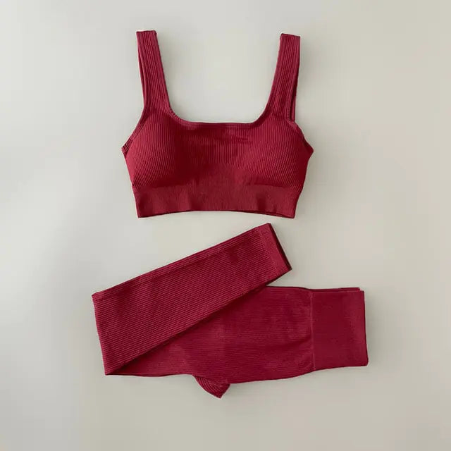 Black ribbed sports bra and matching high-waisted leggings set laid flat on a neutral gray background. The outfit is designed for activewear or athleisure, featuring a scoop neckline and wide straps on the bra.
