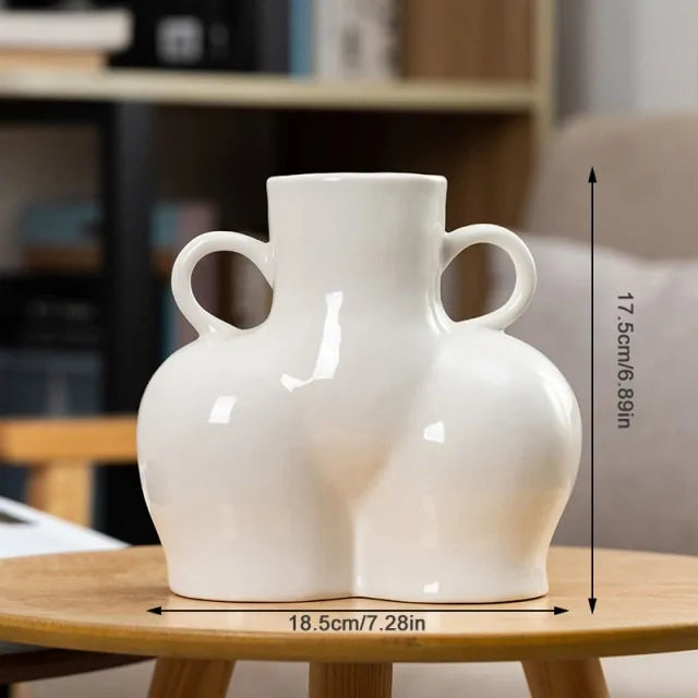 Glossy white ceramic vase shaped like a curvy torso with two small loop handles, placed on a wooden table, with measurements labeled 18.5 cm wide and 17.5 cm tall.