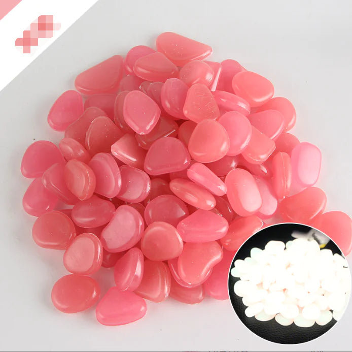 A close-up image of small, smooth, pink-colored pebble-like items arranged together. Some white-colored pebbles are shown in the bottom-right corner of the image for comparison.