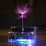A dramatic low-light photo of a tabletop plasma-style display: a clear acrylic box base with blue underglow and control knobs, topped by a thin vertical metal rod that emits branching purple electric arcs forming a tree-like corona against a dark background.