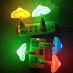 A dimly lit photo of several mushroom-shaped LED night lights plugged into wall power strips, glowing in different colors (yellow, green, blue, and red) and casting colorful light on the surrounding wall.