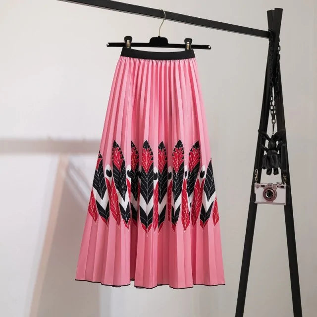 Pleated midi skirt with a gradient design, transitioning from dark black at the waistband to a soft blush pink at the hem, hanging on a black clothing rack next to a vintage-style camera.