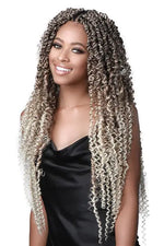 Smiling woman wearing long, tight-curly twist/braided hair extensions in an ombré color from dark brown at the roots to blonde at the ends, styled with a center part and draping past the chest, against a white background.