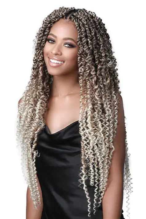 Smiling woman wearing long, tight-curly twist/braided hair extensions in an ombré color from dark brown at the roots to blonde at the ends, styled with a center part and draping past the chest, against a white background.