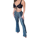 Woman wearing a black crop top and high-waisted, flared bohemian print pants with a mix of geometric and floral patterns in shades of purple, white, and maroon, posing with one hand on her hip