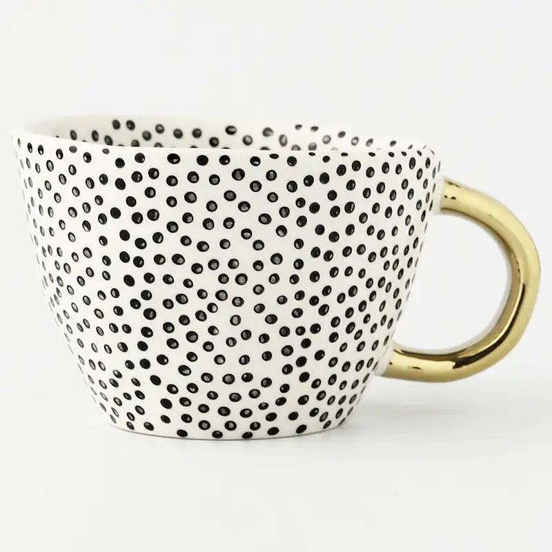 White ceramic mug covered in small black polka dots with a shiny gold handle, shown on a white background.
