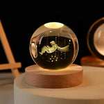 A glowing crystal ball with an engraving of a child sitting in the air with a flowing cape, surrounded by stars, placed on a wooden base. The ball emits a soft light from within.