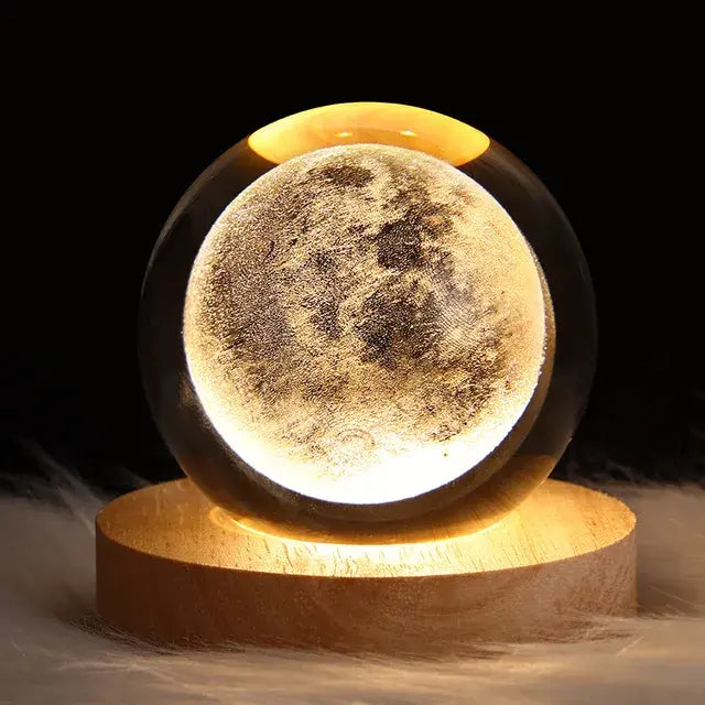 Illuminated crystal ball engraved with a detailed full moon, sitting on a round wooden lighted base against a dark background.