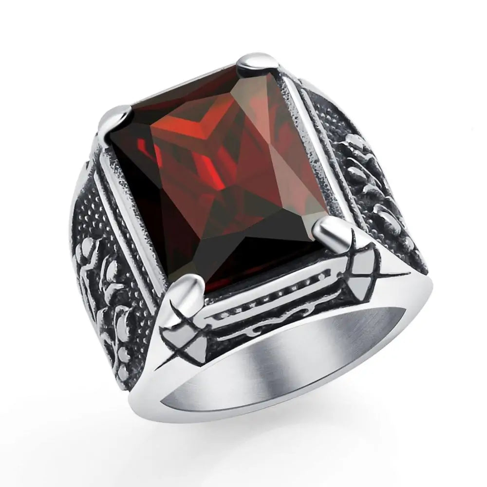 Silver-toned statement ring with a large faceted square red gemstone, held by four prongs, and dark engraved detailing on the sides, shown on a white background.