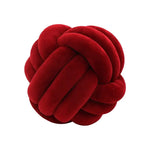 Deep red plush knot pillow made of thick braided tubes, shown against a white background.